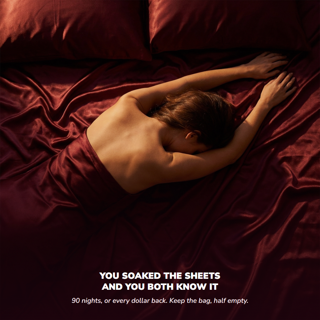 A woman lying on rumpled burgundy satin sheets, seen from above